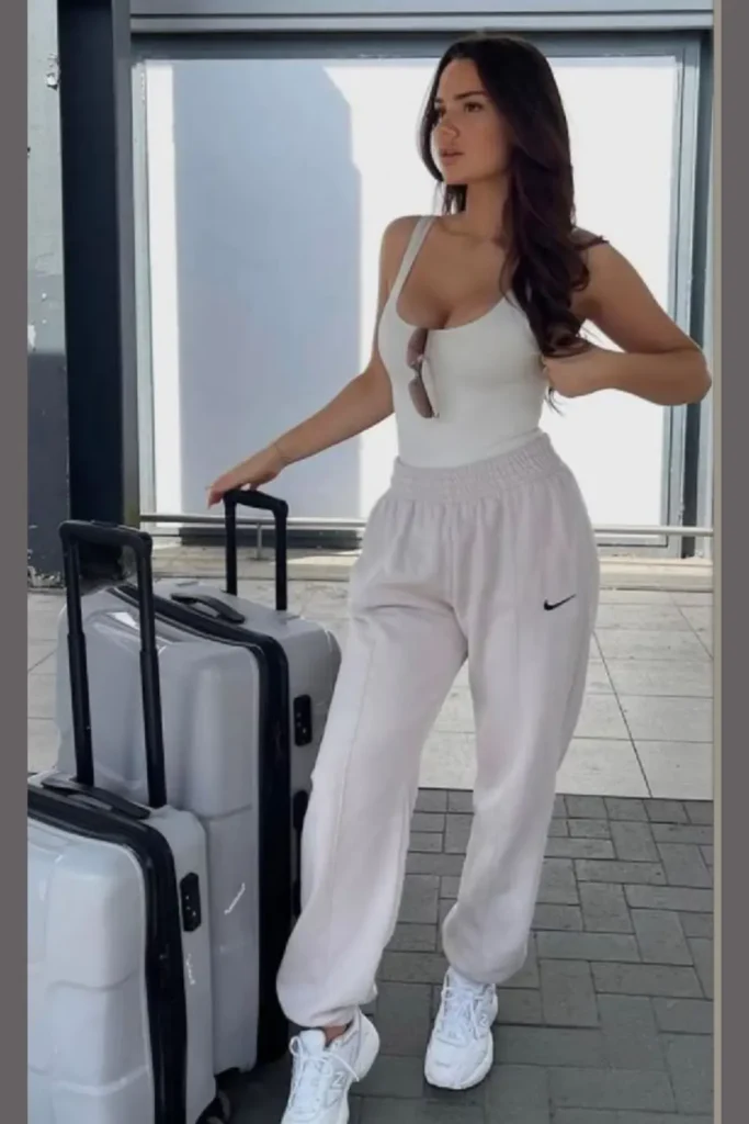 An all-white ensemble with a fitted tank top and relaxed Nike sweatpants. White sneakers tie the outfit together for a comfortable, chic look ideal for travel, seamlessly transitioning from airport to adventure.