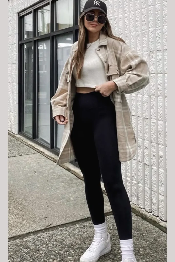 A white crop top paired with black leggings and layered under a neutral plaid oversized shacket. A baseball cap and white sneakers enhance the sporty vibe, while visible white socks add a trendy touch. Ideal for coffee runs or casual meetups.