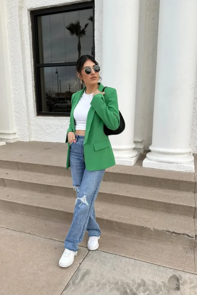 Statement fashion with a vibrant green blazer, white crop top, distressed jeans, and white sneakers. A perfect mix of sophistication and comfort for an effortlessly trendy city look.