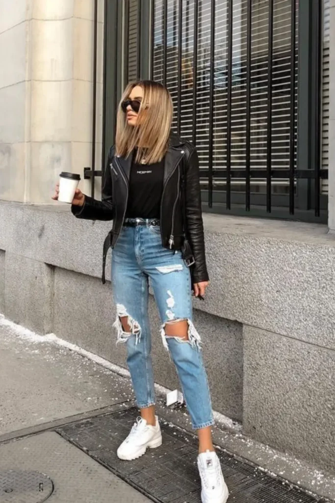 A classic leather jacket paired with distressed jeans creates a timeless, cool-girl look. A simple black top and chunky white sneakers complete the practical yet stylish outfit perfect for a coffee run.