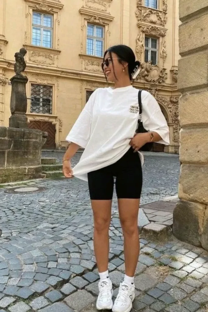 Casual European street style featuring an oversized white tee, bike shorts, and white sneakers. The cobblestone streets and historical architecture add a timeless charm to this effortlessly chic outfit.