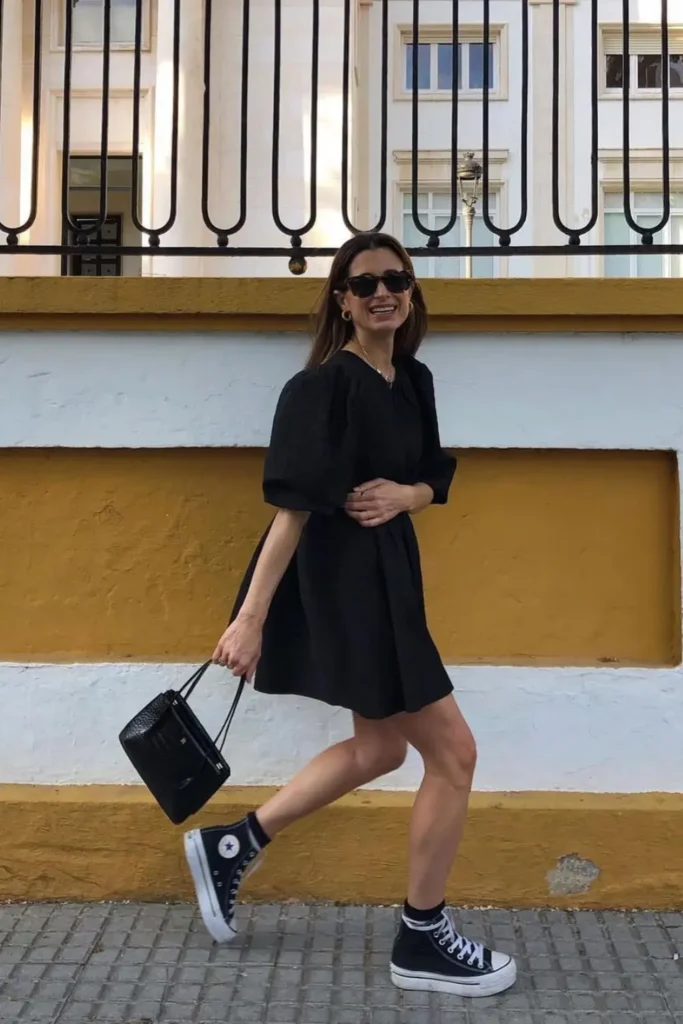 Effortlessly edgy look with a black mini dress and black high-top sneakers. The sleek black handbag adds sophistication, making this the perfect casual-chic outfit for date nights or dinner with friends.