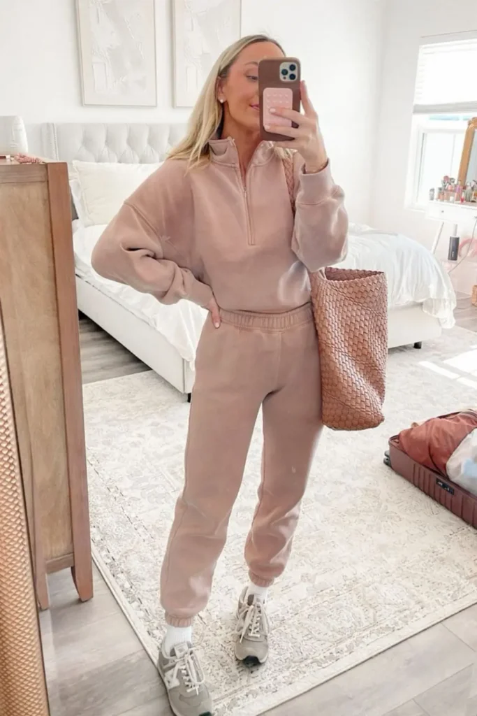 A blush pink half-zip sweatshirt and joggers create a cozy yet stylish loungewear look. Neutral sneakers and a woven tote bag add effortless chic, perfect for errands or relaxed outings.