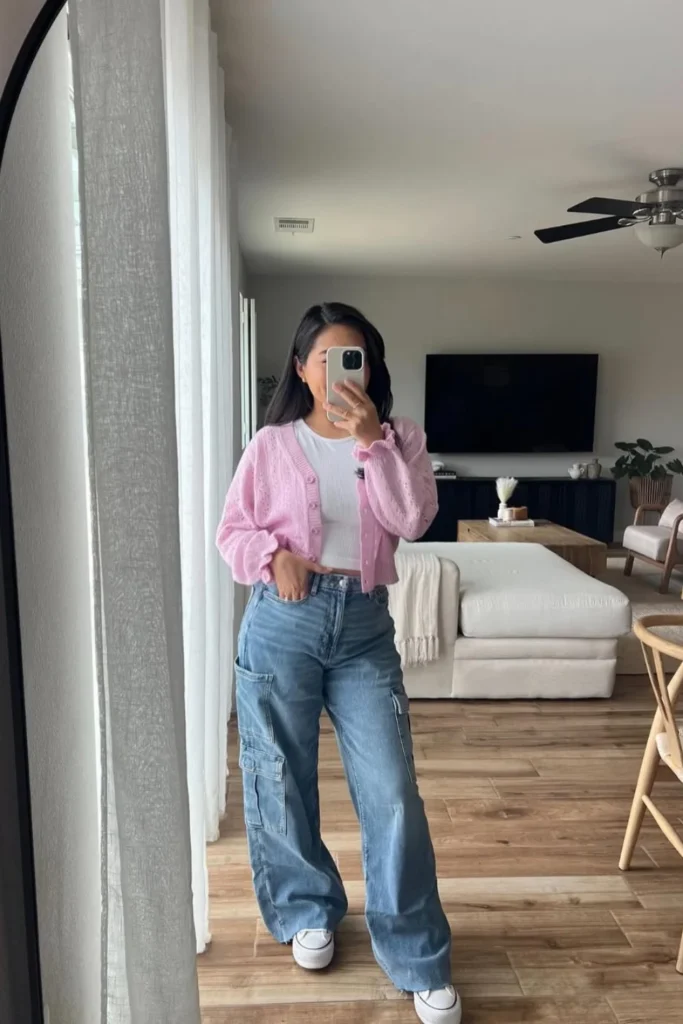 Soft spring style featuring a pastel pink cardigan over a white top, wide-leg blue jeans, and white sneakers. A relaxed yet stylish outfit for coffee runs and shopping days.