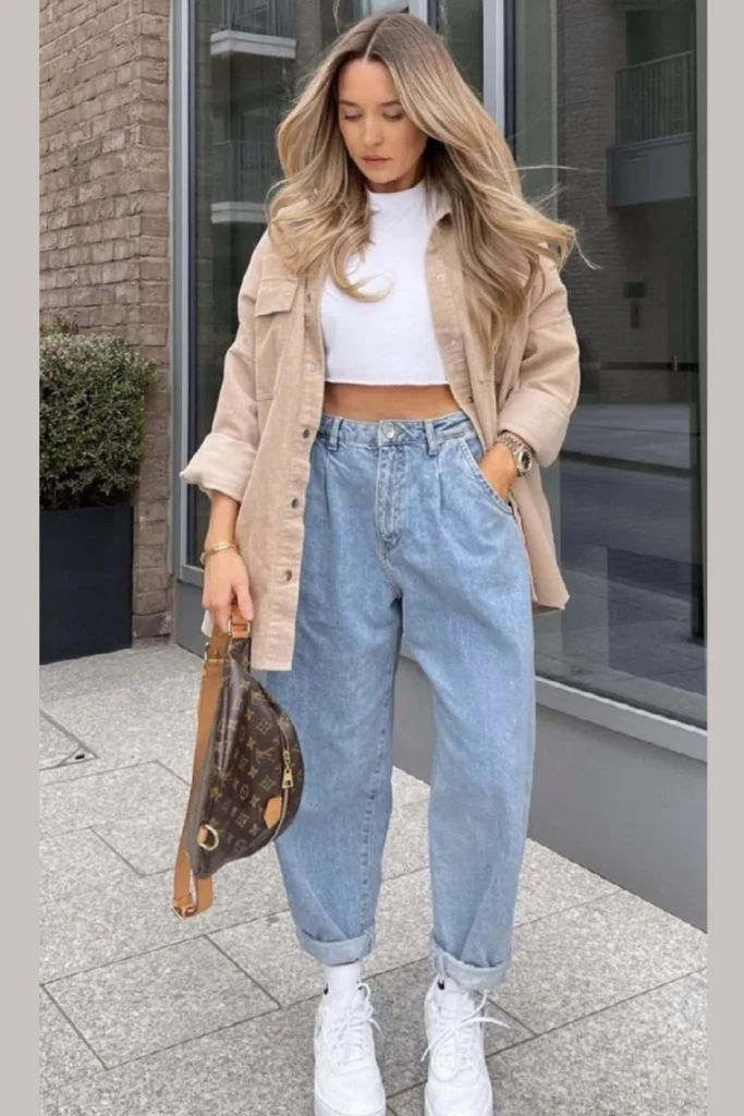 A white crop top paired with light-wash baggy jeans and a beige oversized shacket. The high-waisted jeans balance the cropped top, while the shacket adds warmth and dimension. Completed with a designer belt bag and clean white sneakers, this streetwear-inspired look is perfect for weekend adventures.